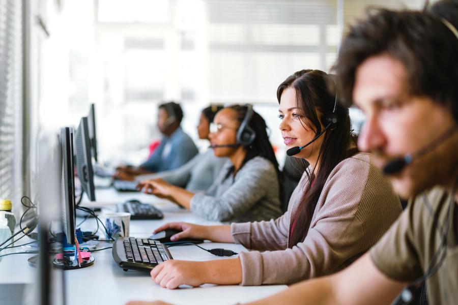 A team of customer service agents, all wearing headsets, seated at a row of computers
