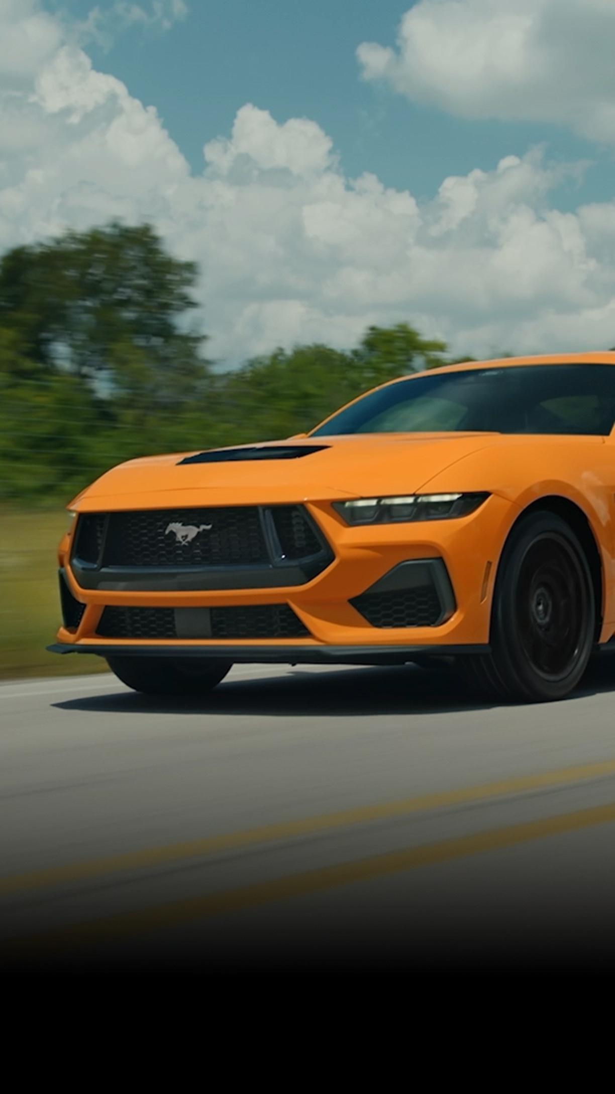 2026 Ford Mustang® GT fastback in Orange Fury Metallic Tri-coat being driven near shipping containers