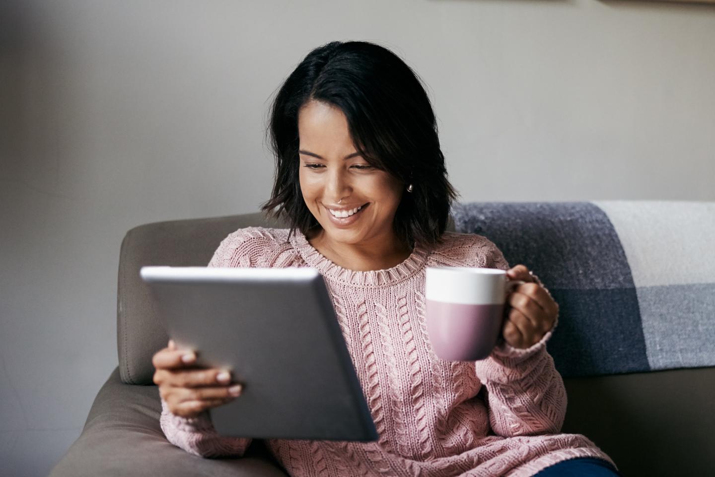 Person seated on a sofa looking at a tablet.
