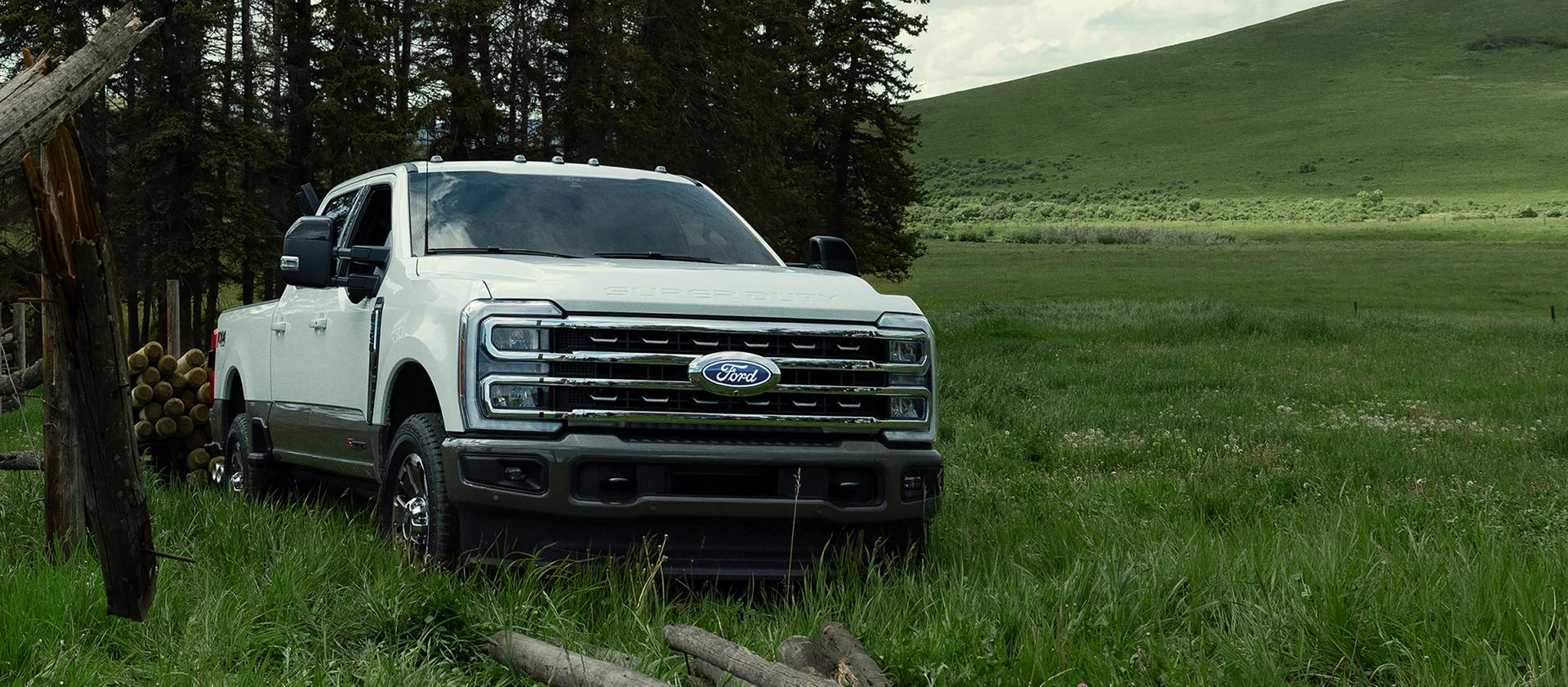 2027 Ford Super Duty® F-350® King Ranch® model pulling a trailer through a grassy field with trees in the background