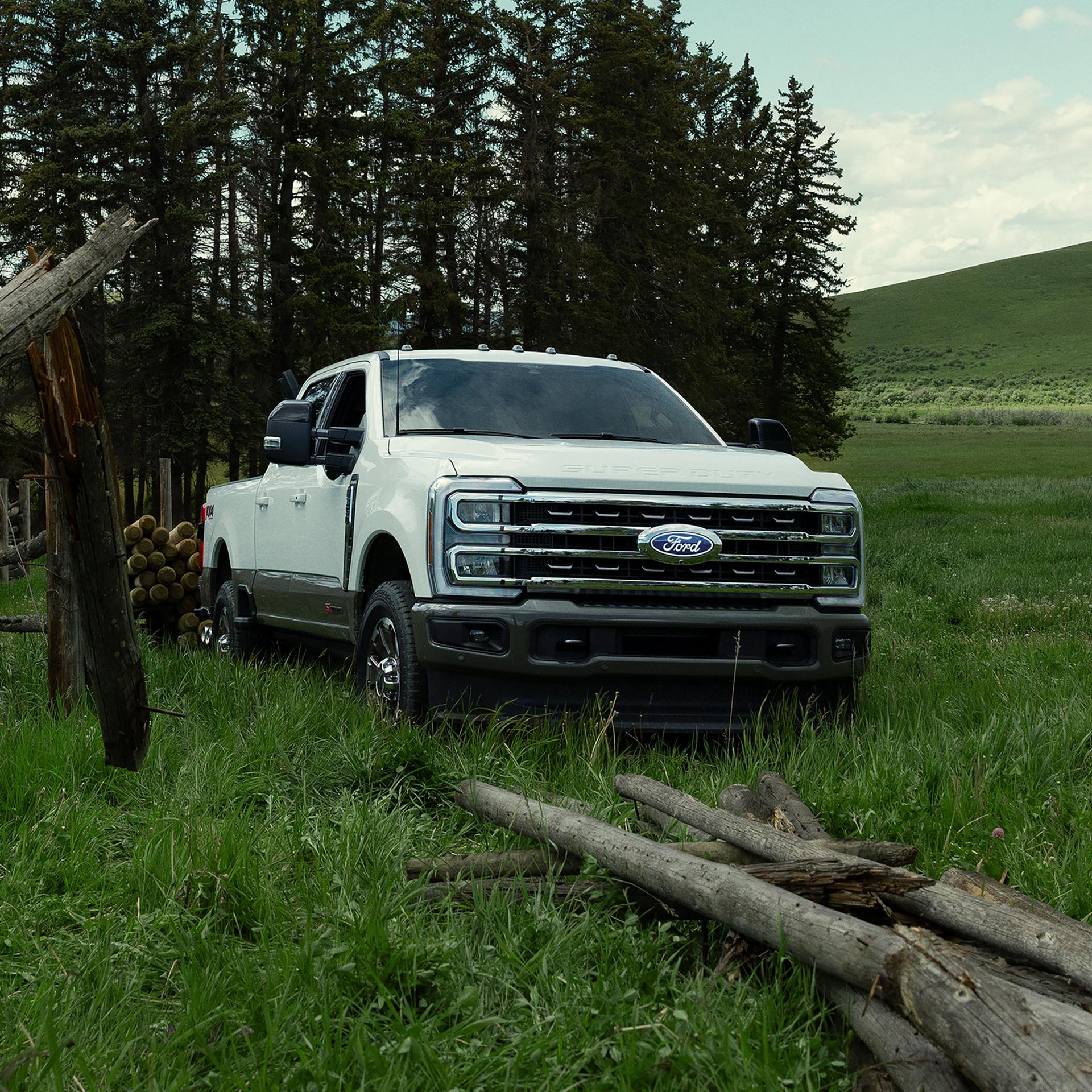 2027 Ford Super Duty® F-350® King Ranch® model pulling a trailer through a grassy field with trees in the background