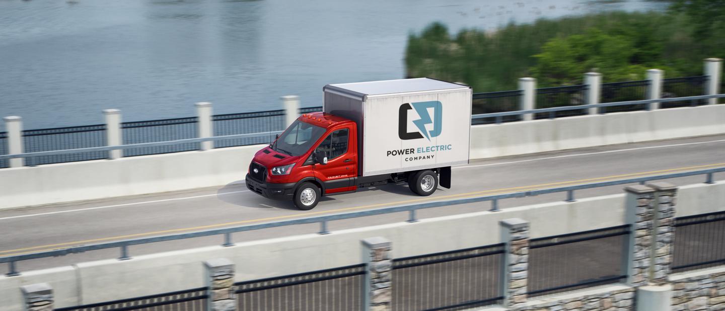 2025 Ford Transit® Chassis Cab model with box truck upfit being driven over a bridge with a lake in the background