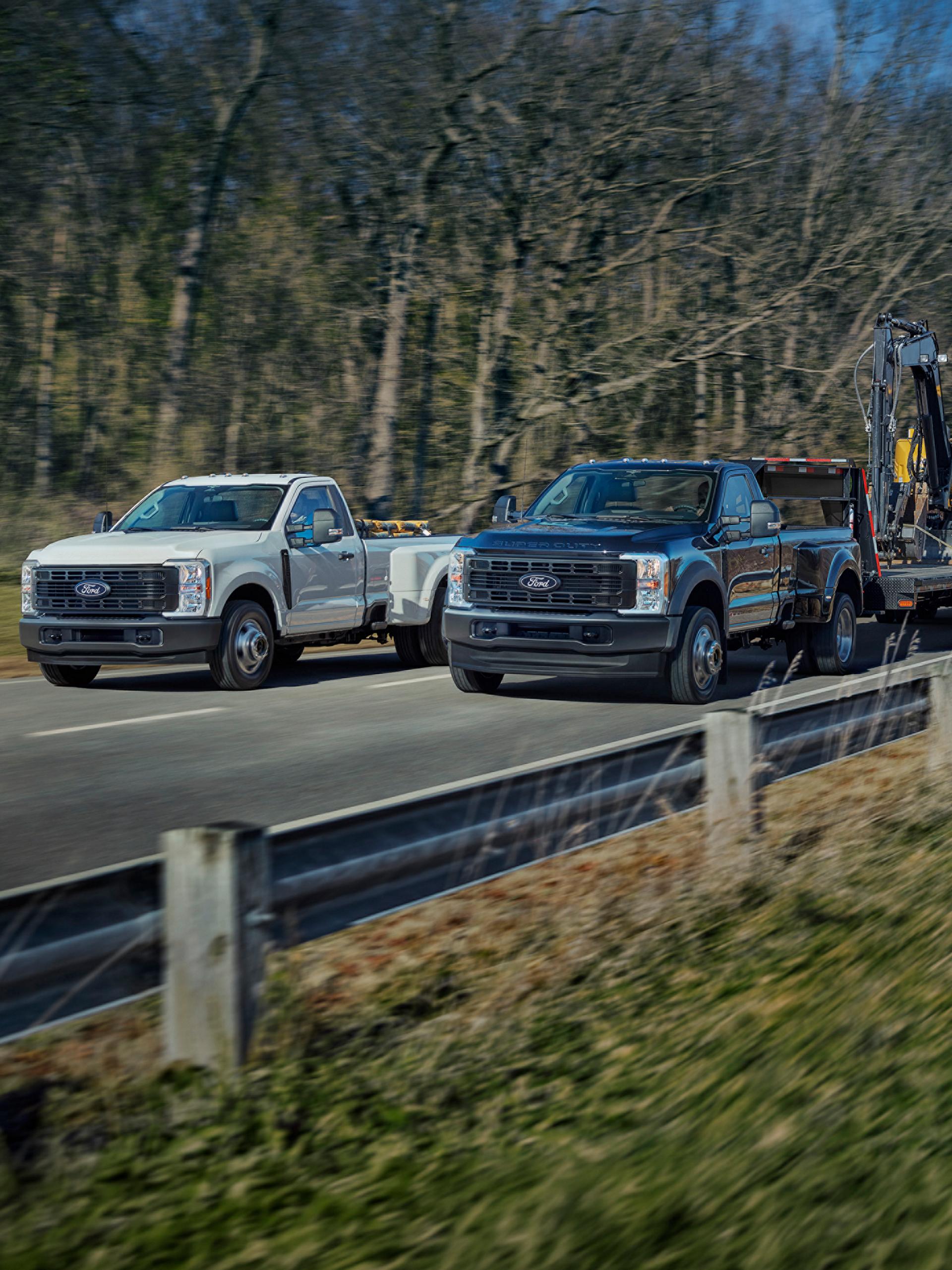 Two 2027 Ford Super Duty® trucks being driven on a paved road. One carries boxes and the other is towing a trailer