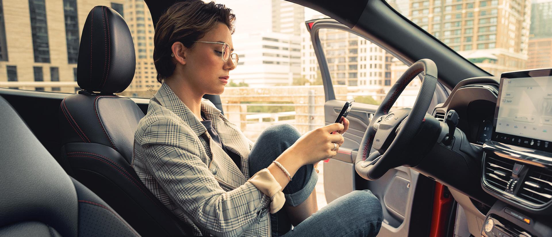 Una persona sosteniendo su teléfono en una SUV Ford Escape® estacionada