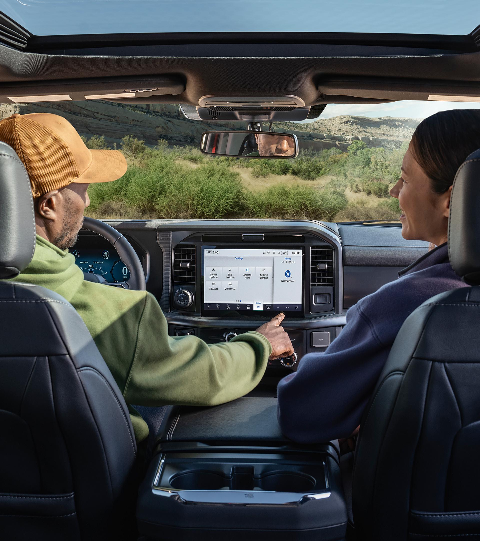 A man using the push-button features on the 12-inch center display with a woman seated in the passenger seat