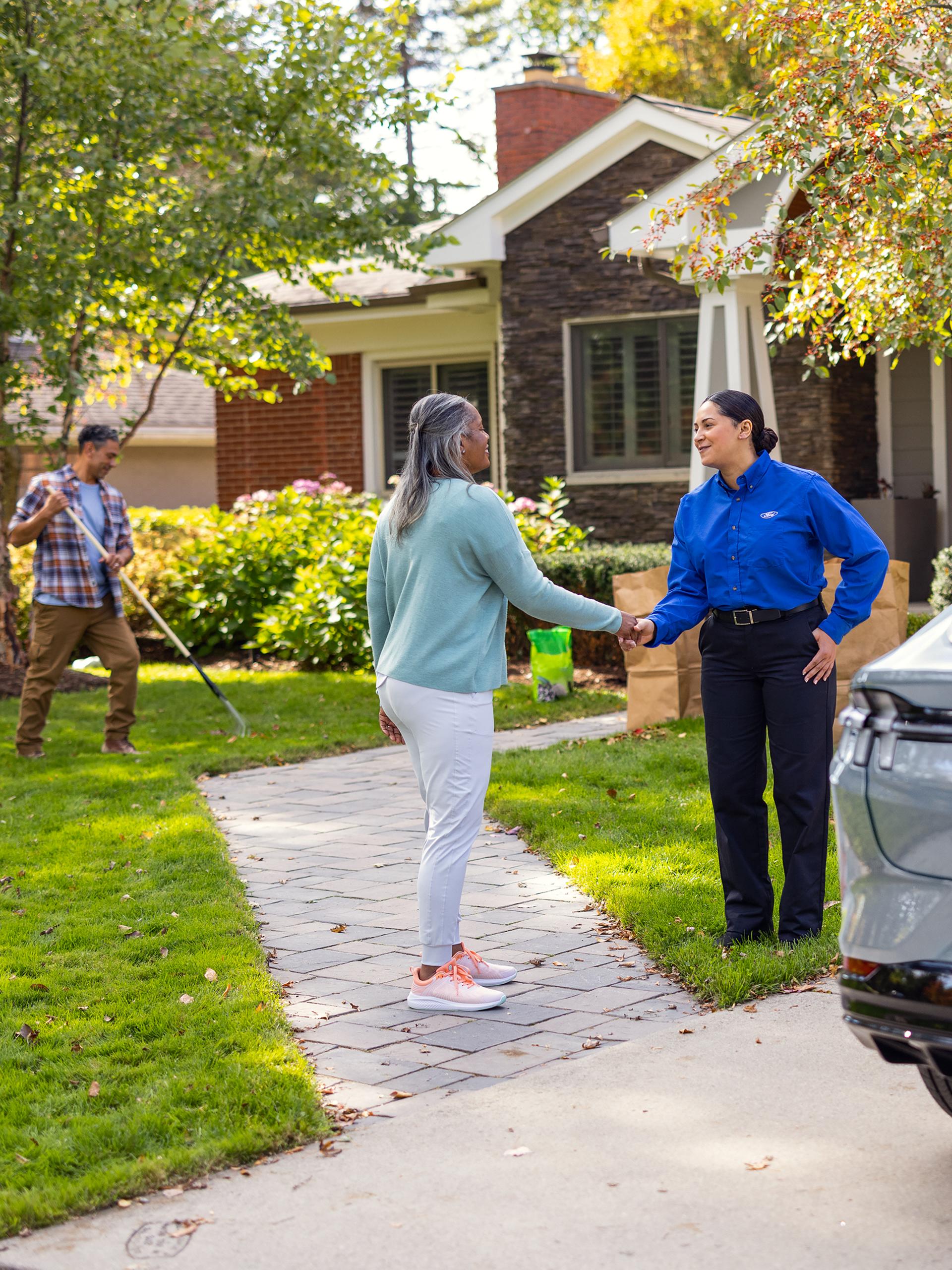 A Ford Service tech exchanges the keys to a Ford Mustang Mach-E® with its owner in the walkway of a home