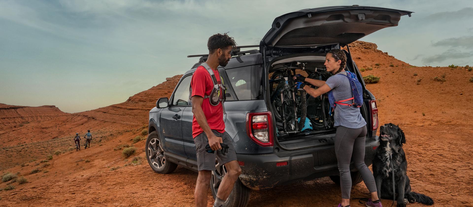 2026 Ford Bronco Sport® parked in the desert with two people standing outside of the vehicle, wearing hiking gear with their dog