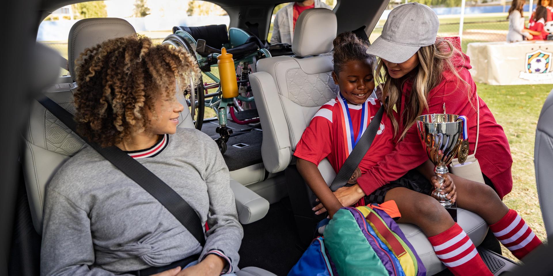 A parent helping secure youth soccer players in the second-row seats of a 2027 Ford Explorer® SUV
