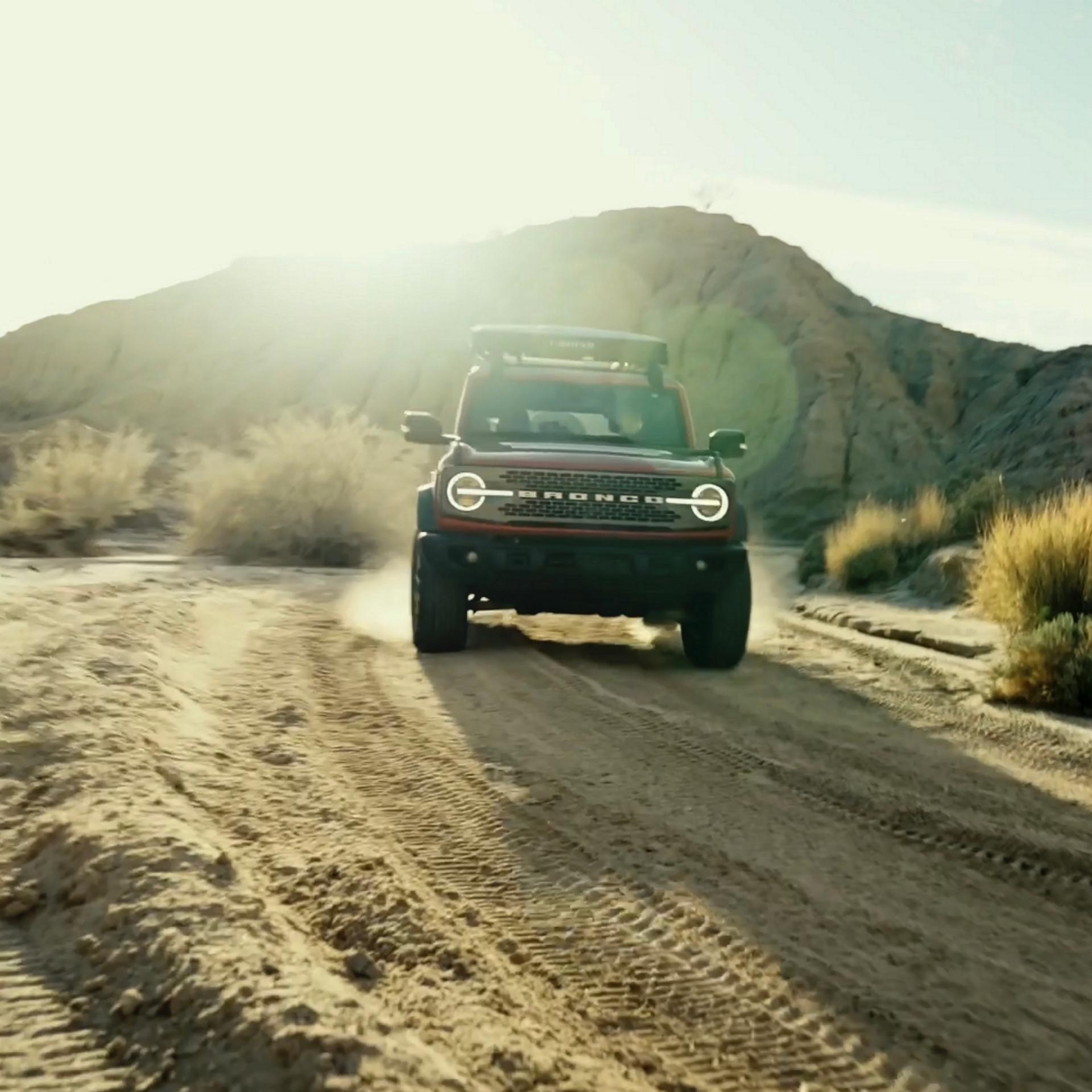 A 2026 Ford Bronco® SUV being driven on a dirt trail through a stark, dusty landscape