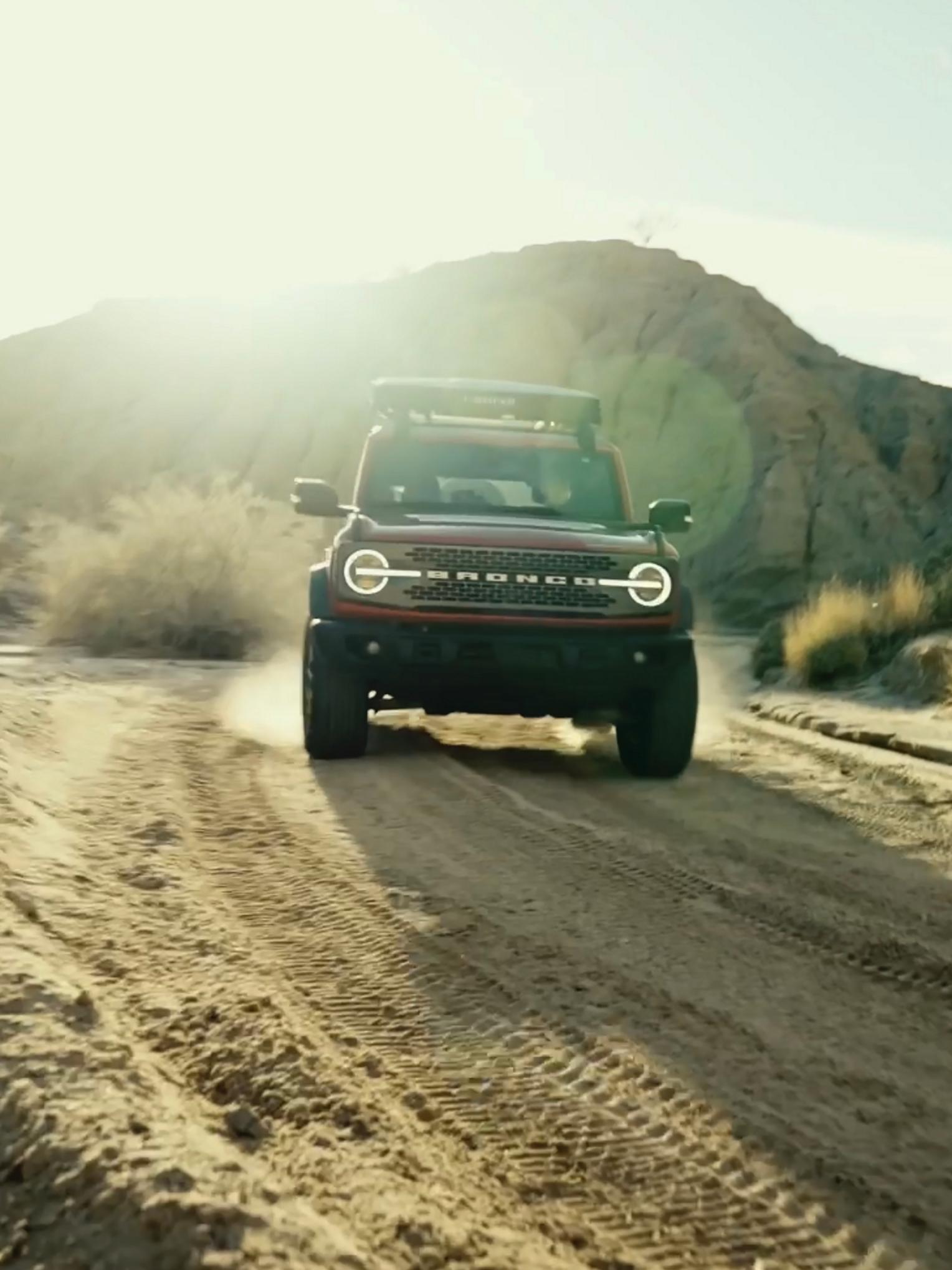 A 2026 Ford Bronco® SUV being driven on a dirt trail through a stark, dusty landscape