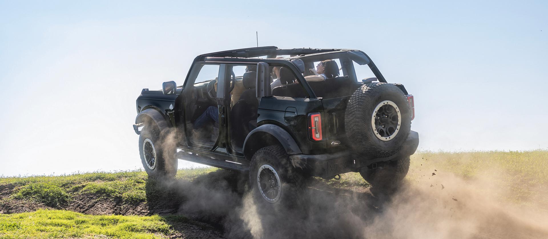 A 2026 Ford Bronco® SUV with the doors removed being driven up a dusty knoll