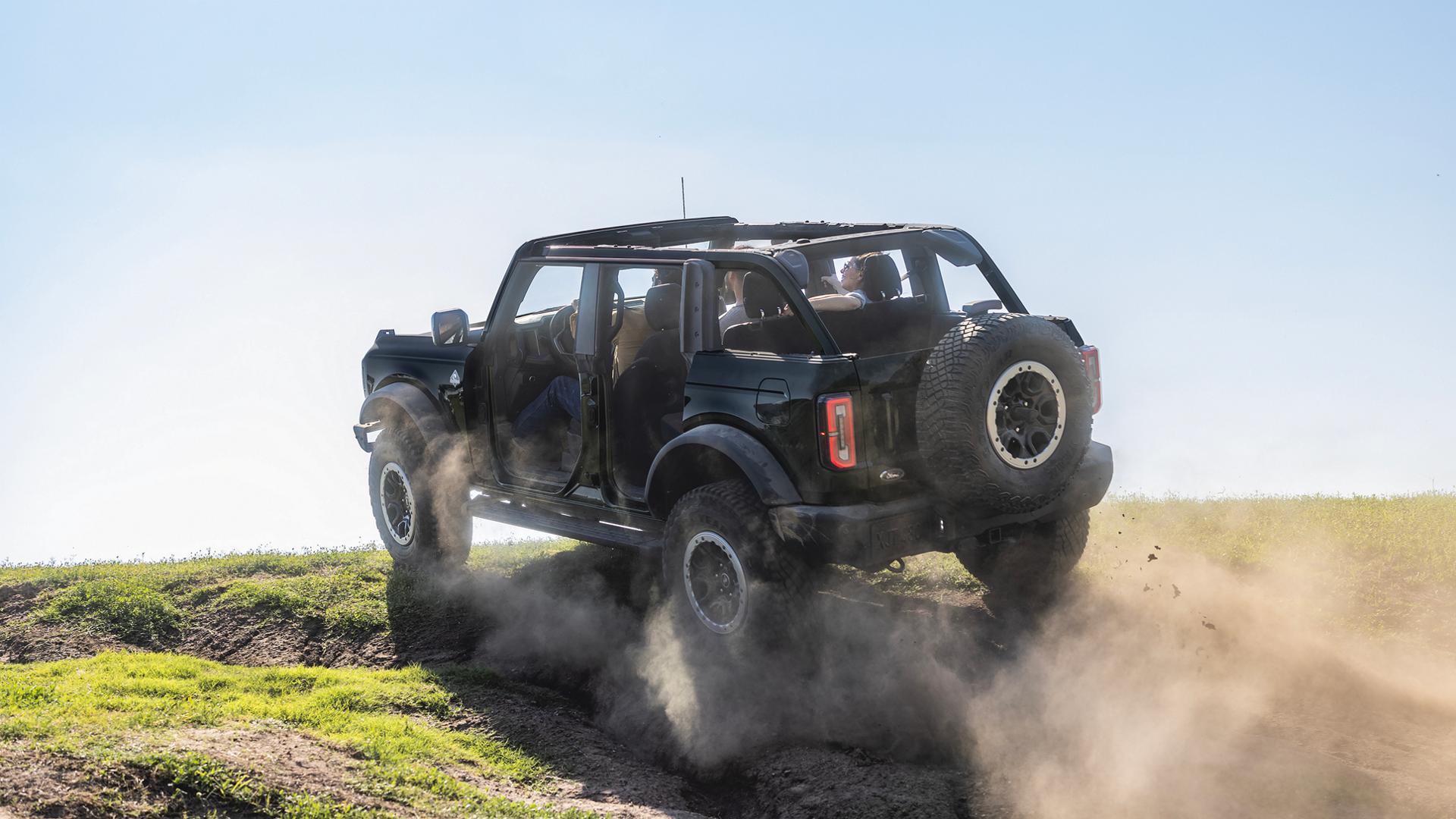 A 2026 Ford Bronco® SUV with the doors removed being driven up a dusty knoll