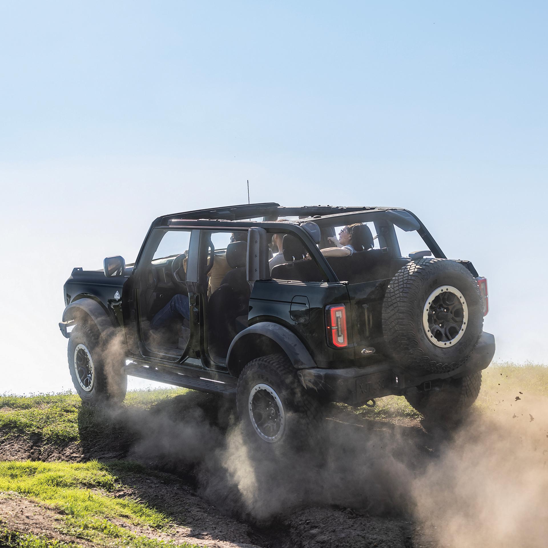 A 2026 Ford Bronco® SUV with the doors removed being driven up a dusty knoll