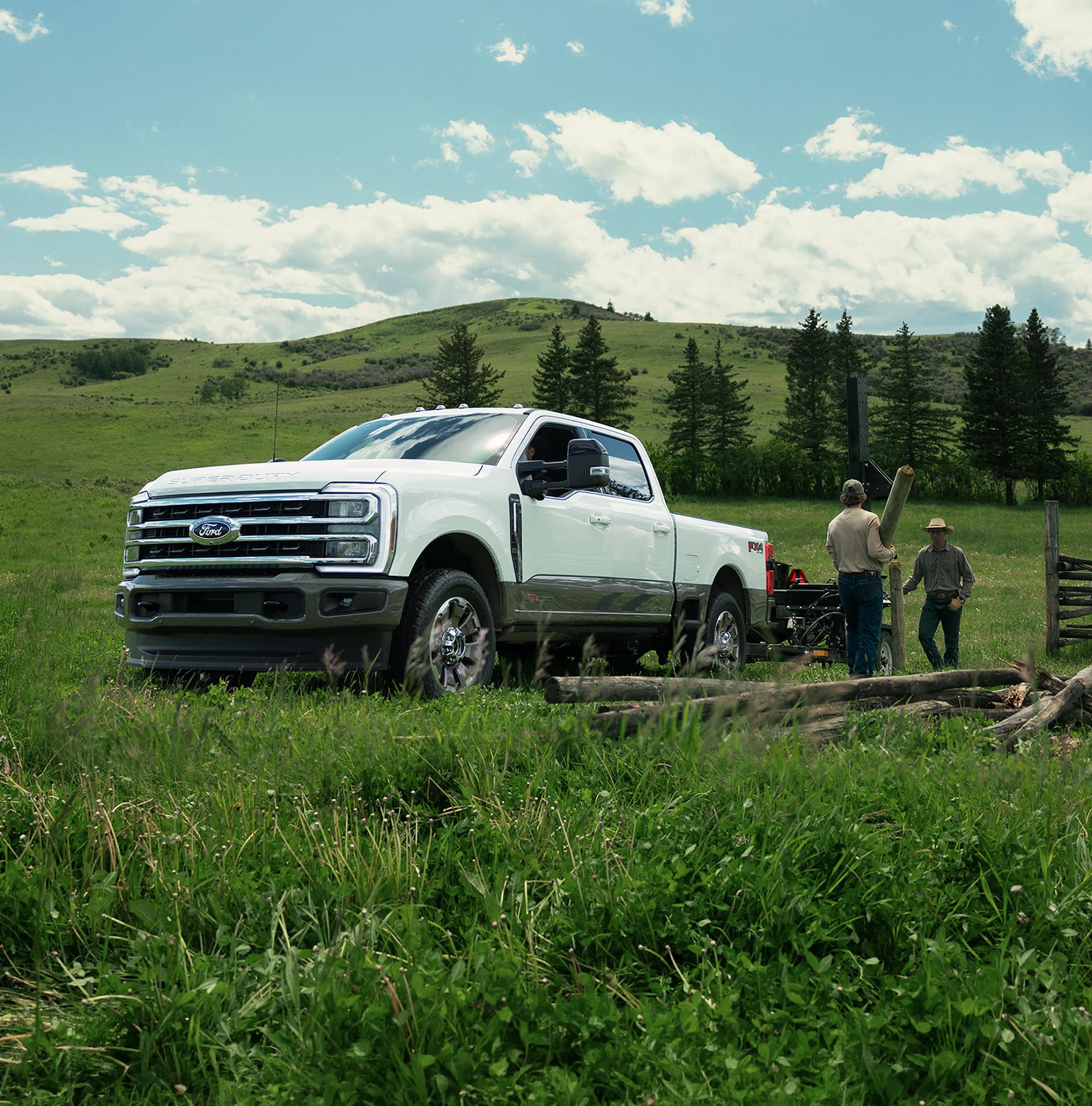2027 Ford Super Duty® F-350® King Ranch® model towing a trailer of lumber with two workers unloading the lumber from the trailer.