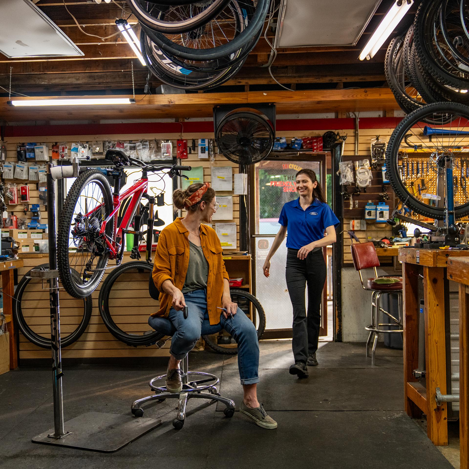 A Ford service tech enters a bicycle shop and picks up keys from an employee