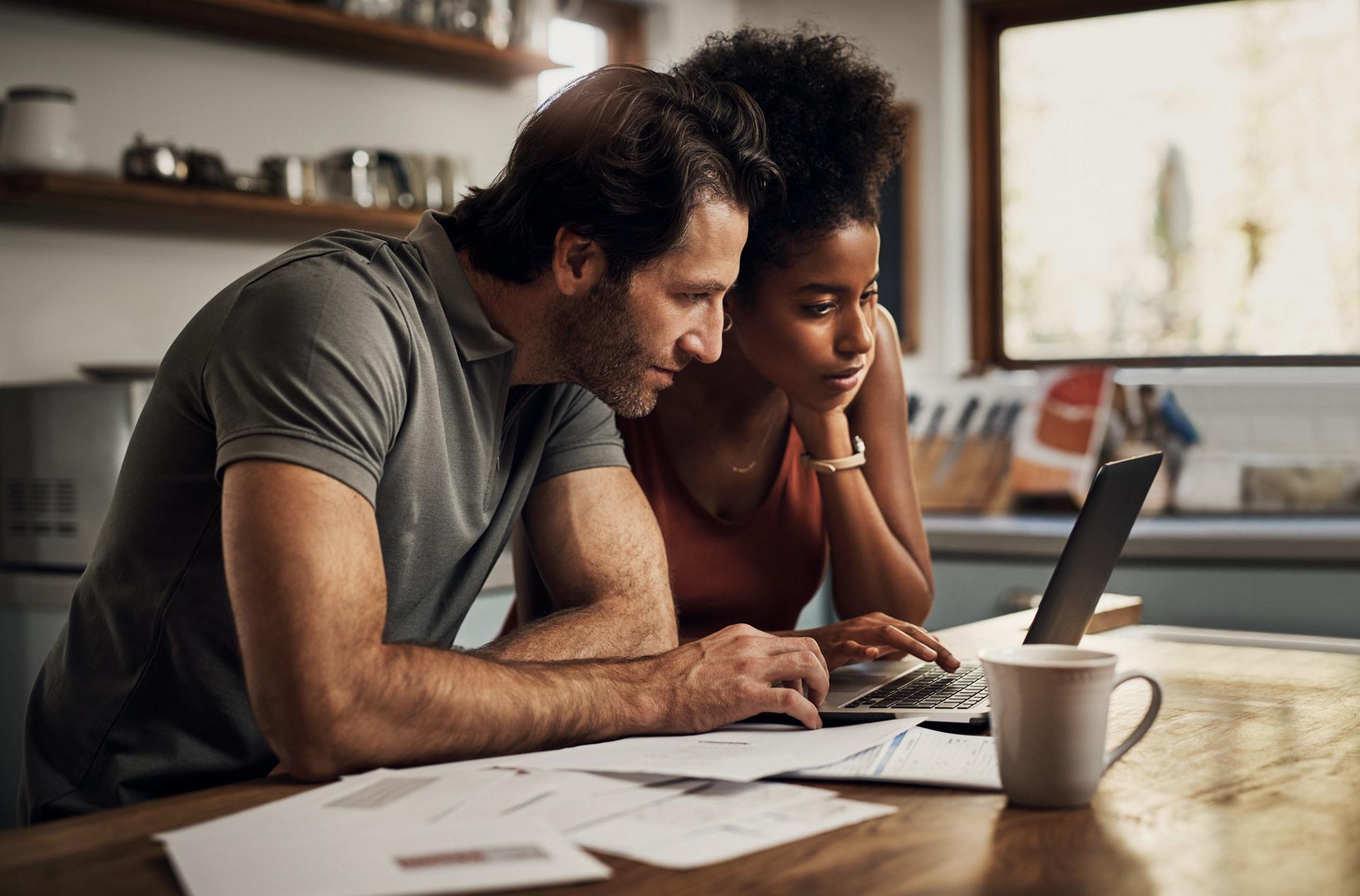 A man and a woman sit side-by-side in front of a laptop computer