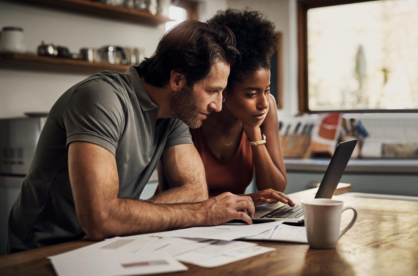 A man and a woman sit side-by-side in front of a laptop computer