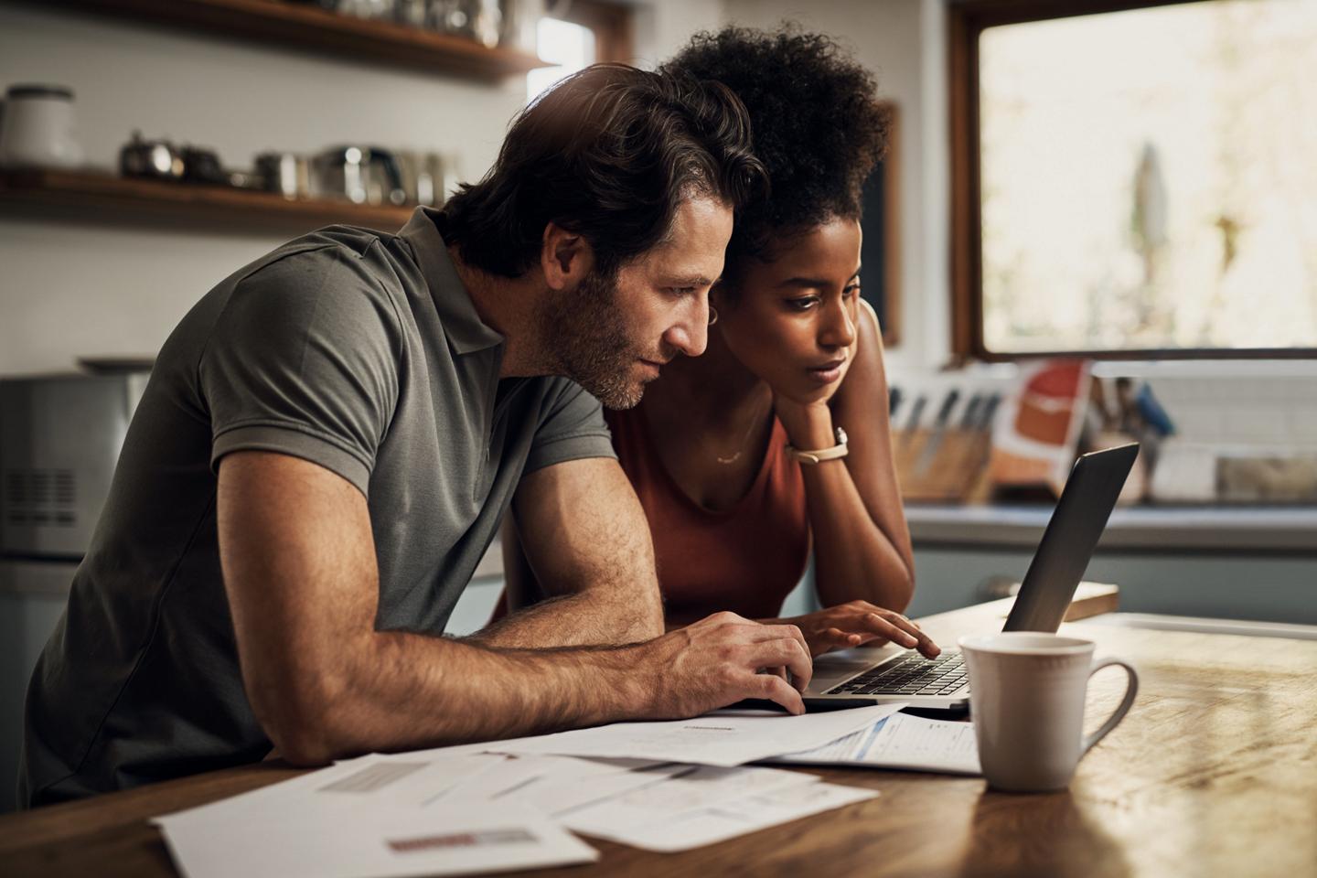 A man and a woman sit side-by-side in front of a laptop computer