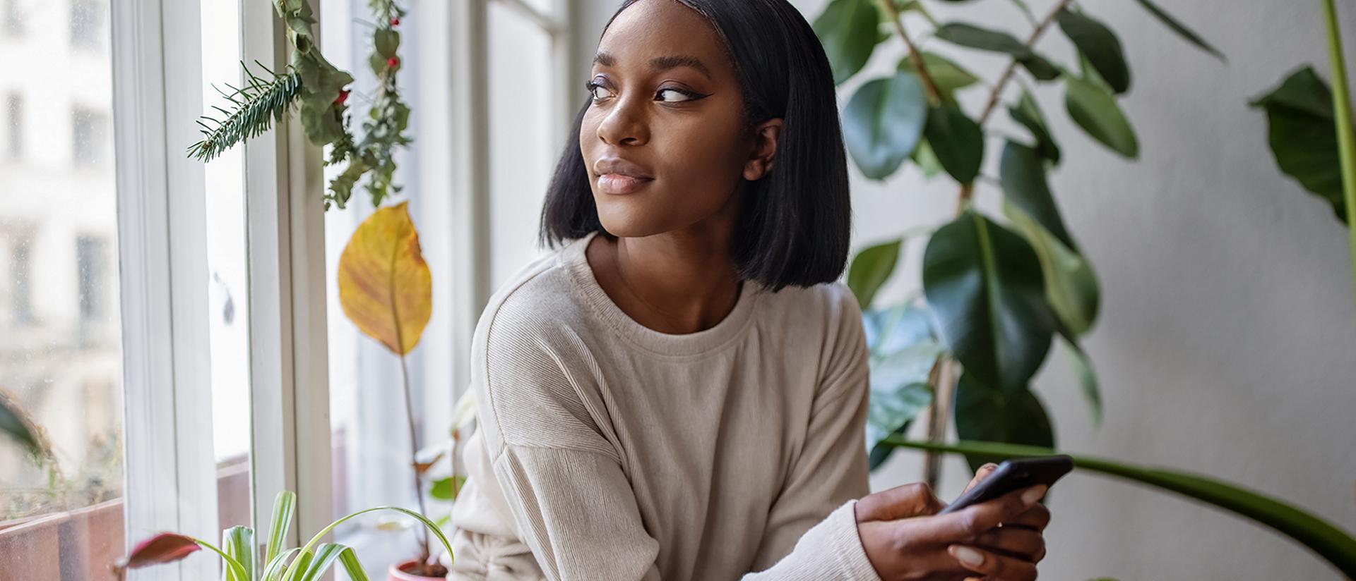 Una mujer sentada cerca de una ventana sosteniendo su smartphone