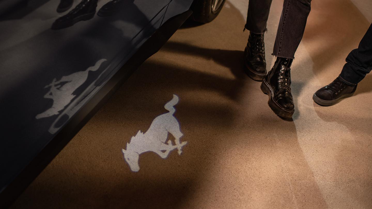 Two people standing near a 2026 Ford Mustang® model with available pony puddle lamps