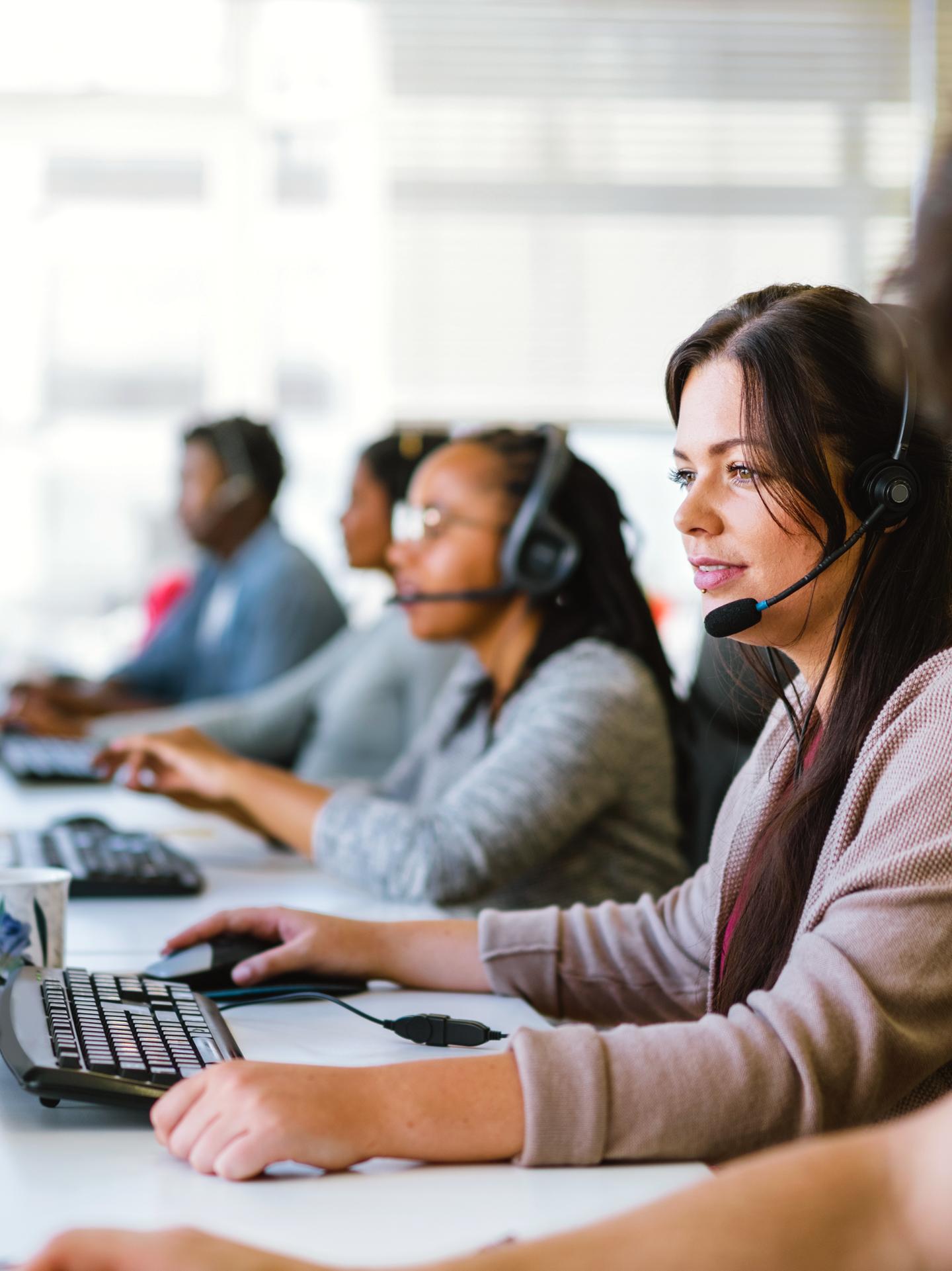 Une équipe d’agents du service à la clientèle, tous portant des casques d’écoute, assis devant une rangée d’ordinateurs