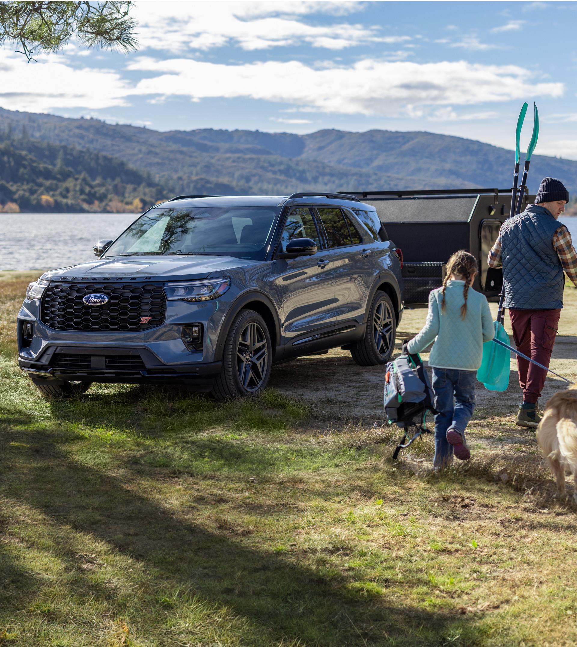 A parent walks with their child and dog past a Ford Explorer® SUV toward the lake