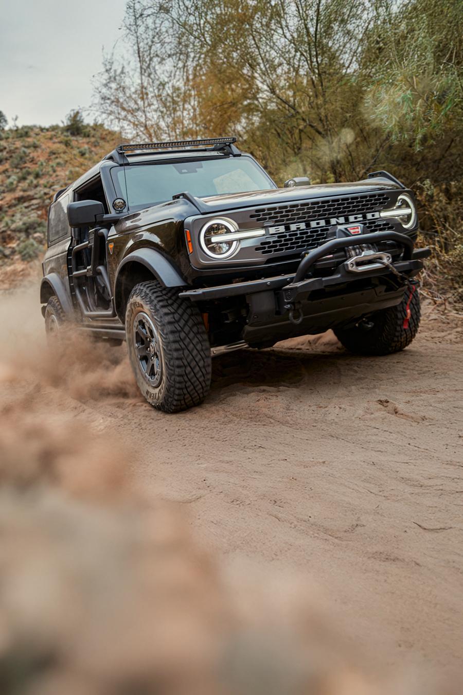 A black 2024 Ford Bronco® SUV being driven through mountainous terrain. Dust is being kicked up.