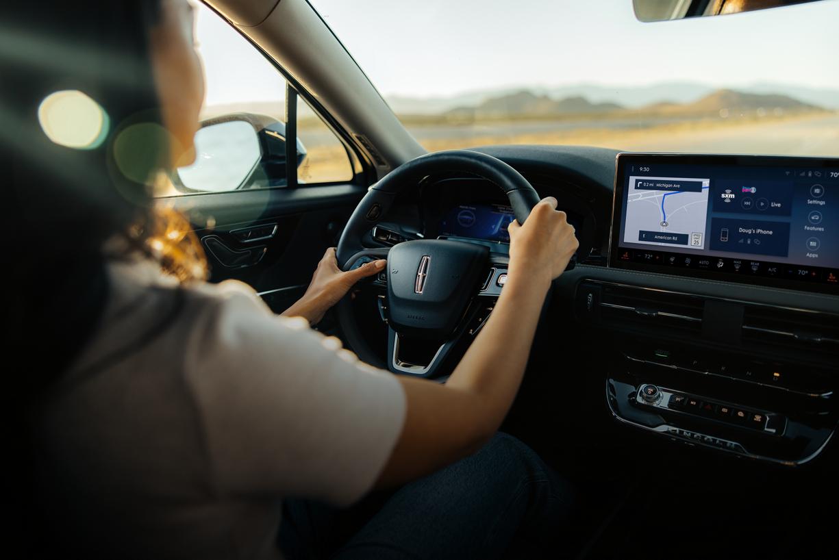 A woman is shown driving a Lincoln vehicle hands-free using Lincoln BlueCruise on a highway.