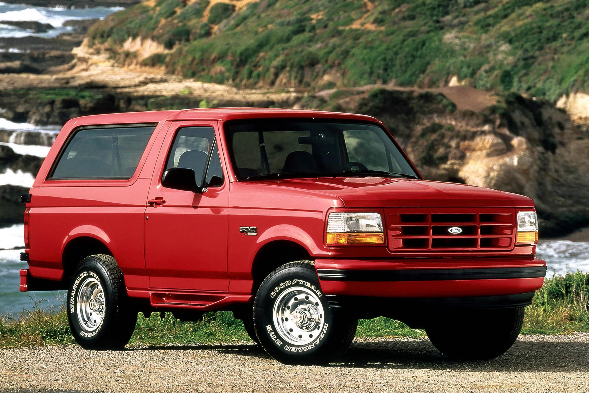 A red 1995 Ford Bronco® model parked in front of a coastal terrain