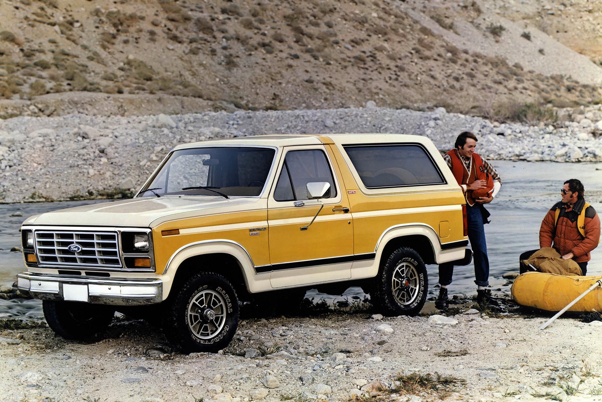 A two-tone 1982 Ford Bronco® model parked at a river with two white water rafters