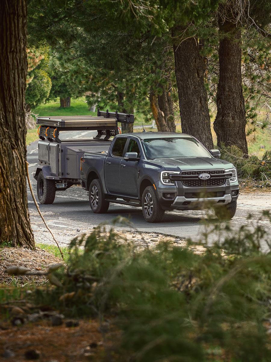 A 2025 Ford Ranger® in Cactus Gray towing a trailer through a wooded road