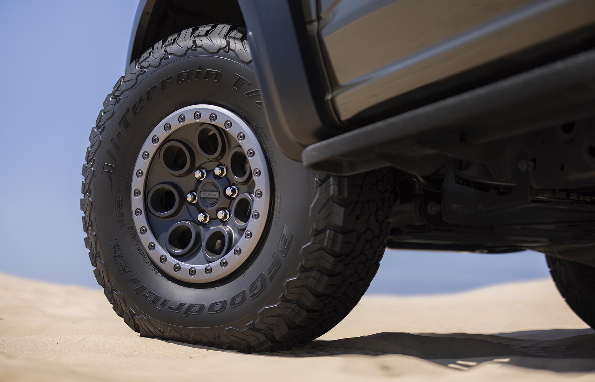 A close-up view of a rugged all-terrain tire and wheel, showing the aggressive, mud-shedding tread