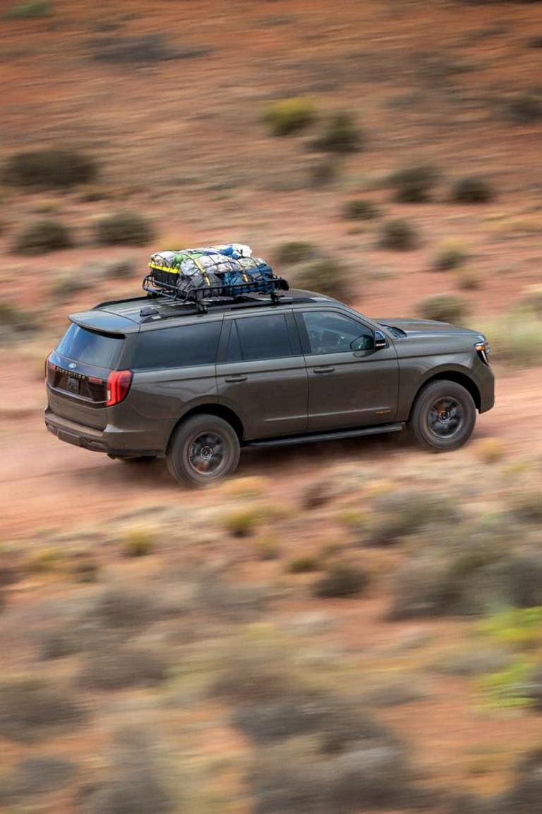 A gray 2025 Ford Expedition Tremor model driving on a dirt road in a desert setting with gear secured on top