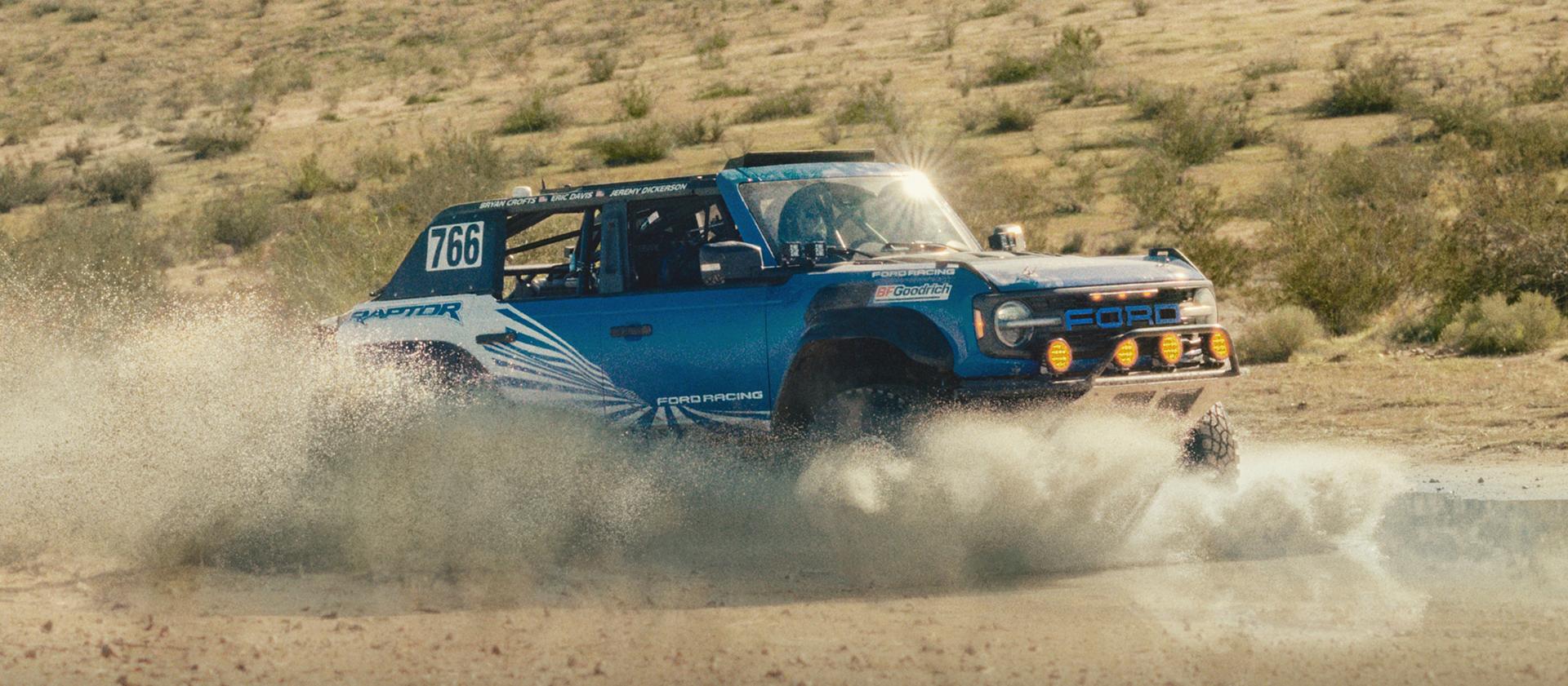 A blue with white graphics 2025 Ford Bronco® Raptor® racing through the desert
