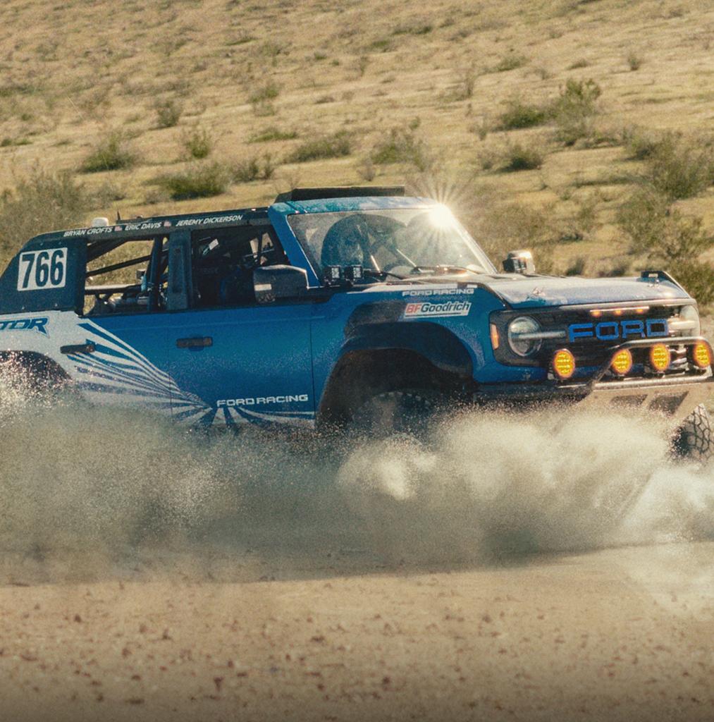A blue with white graphics 2025 Ford Bronco® Raptor® racing through the desert