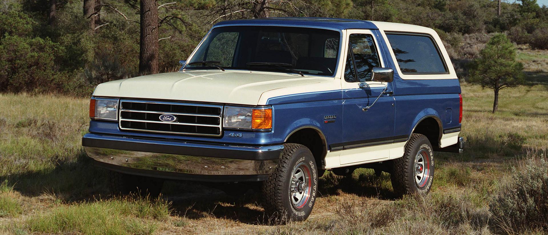 A two-tone blue and white 1989 Ford Bronco® model parked on a tree-lined trail