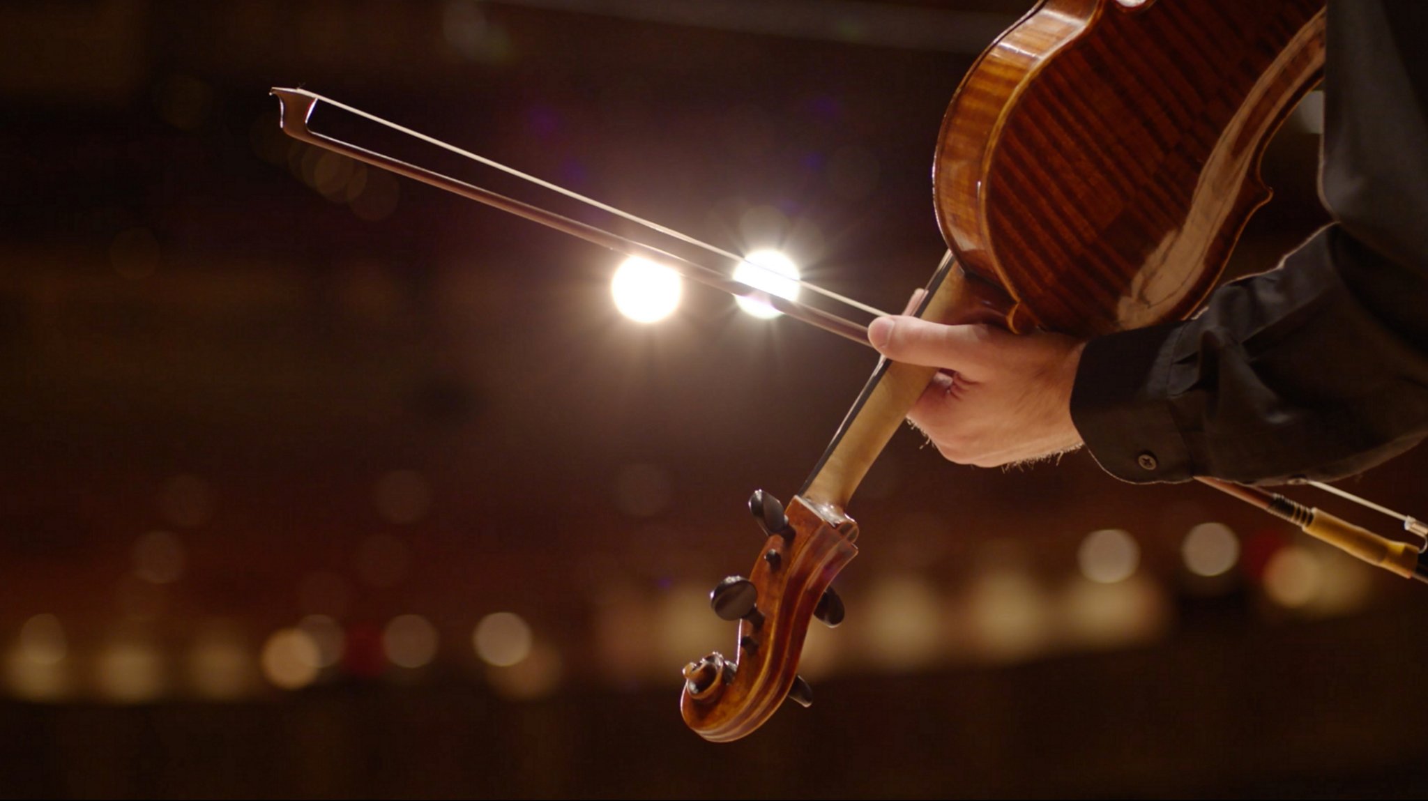 A person draws a bow across the string of a violin alluding to the chimes in a 2026 Lincoln Corsair