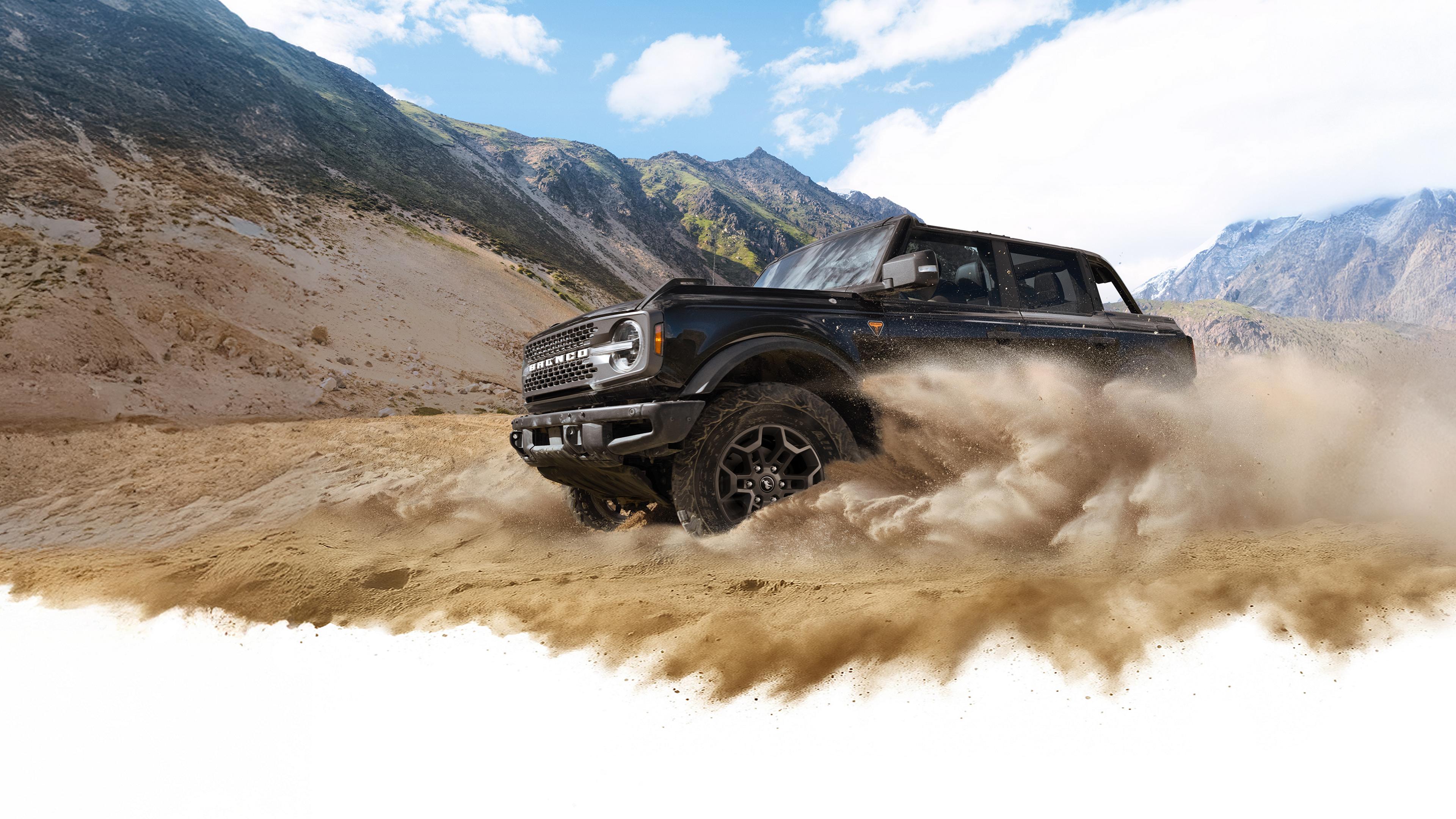 A 2026 Ford Bronco® SUV kicking up dust in a valley beneath rocky hills