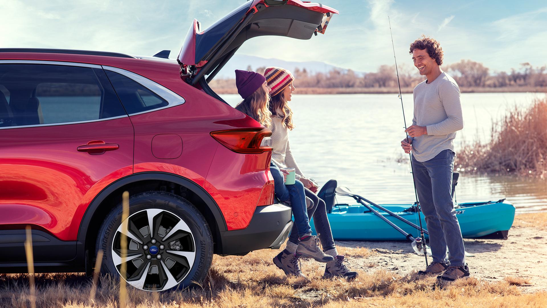 By the lake, two friends sit on the tailgate of their Ford vehicle while another stands nearby