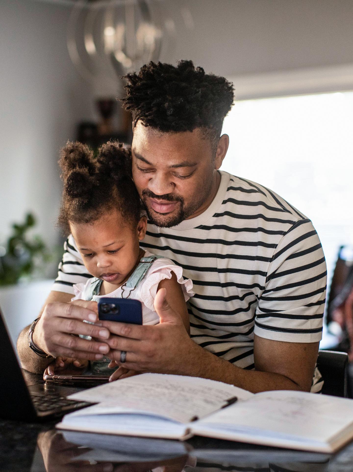A man holds his child in his lap while interacting with the FordPass app on his phone