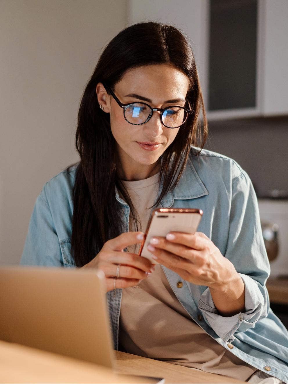 A woman sitting at a desk and looking at a cell phone.