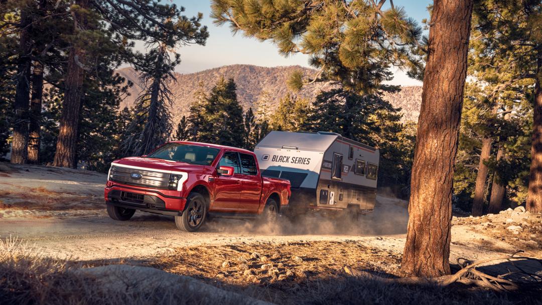 A 2025 Ford F-150® Lightning® hauling a camper on a dirt road in a scenic location