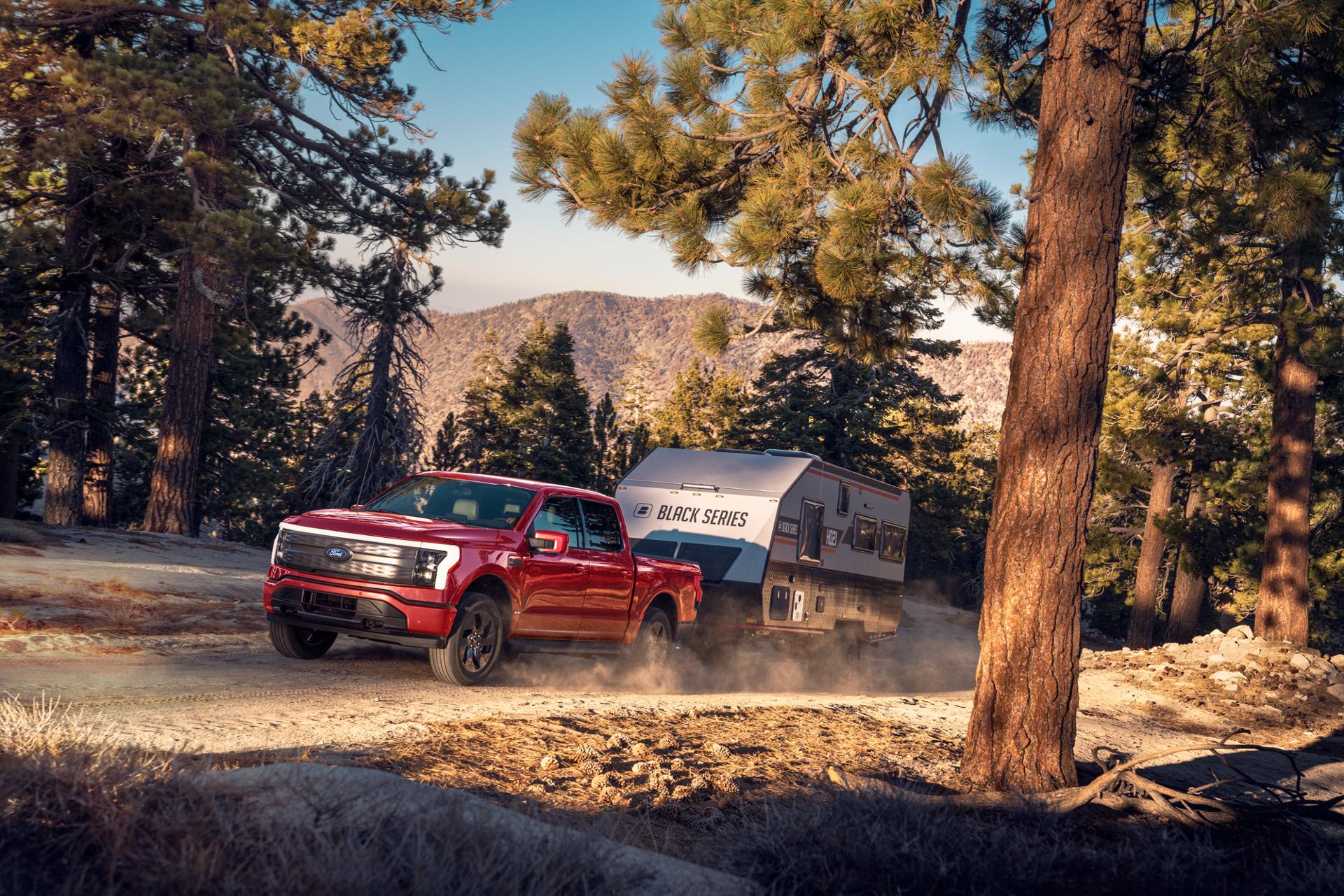 A 2025 Ford F-150® Lightning® hauling a camper on a dirt road in a scenic location