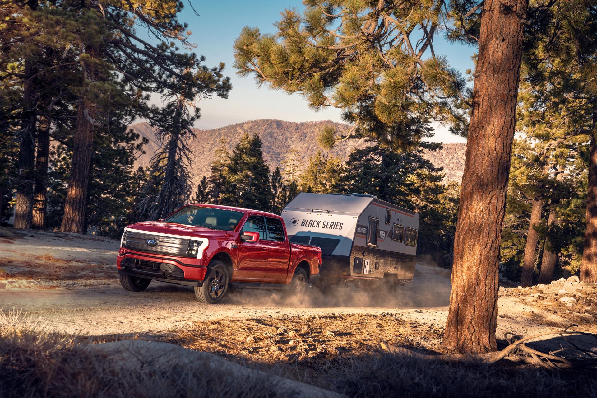 A 2025 Ford F-150® Lightning® hauling a camper on a dirt road in a scenic location