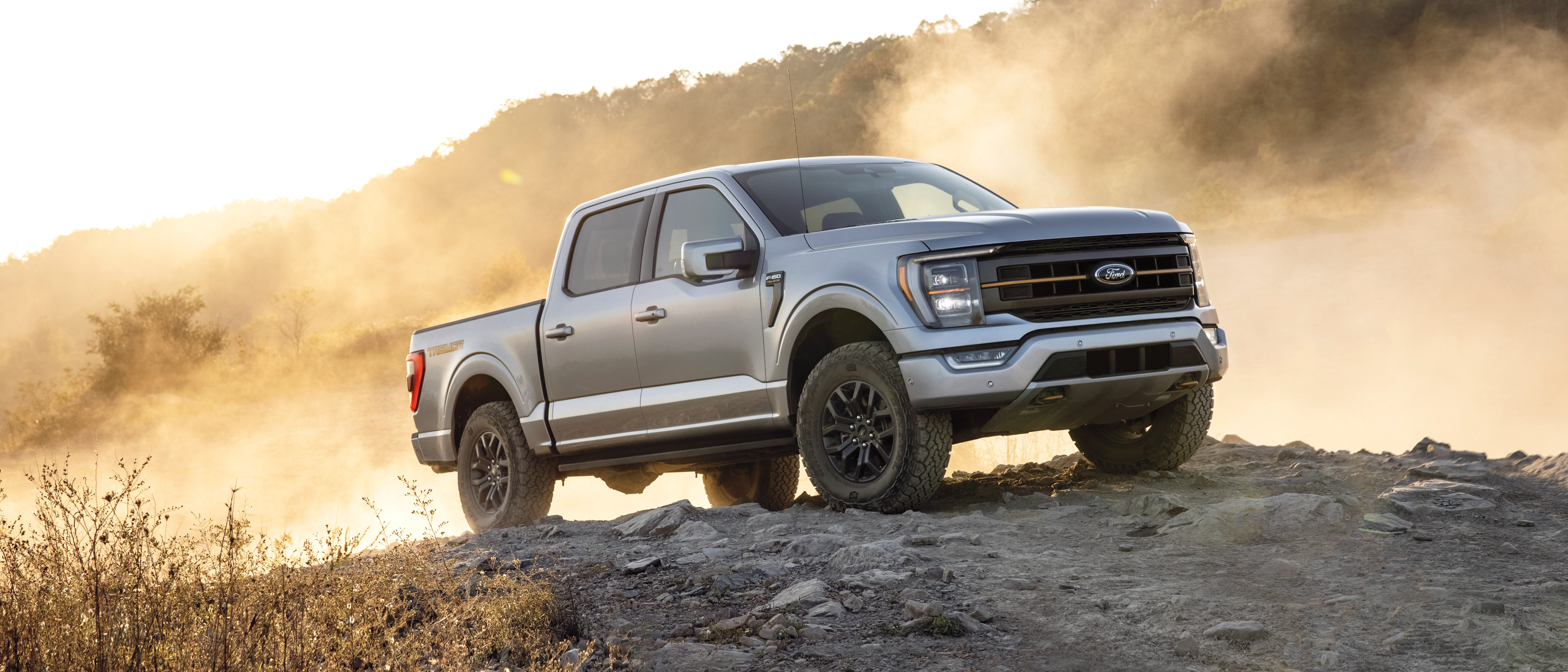 A Ford F-150 parked on rocky terrain with dust in the background