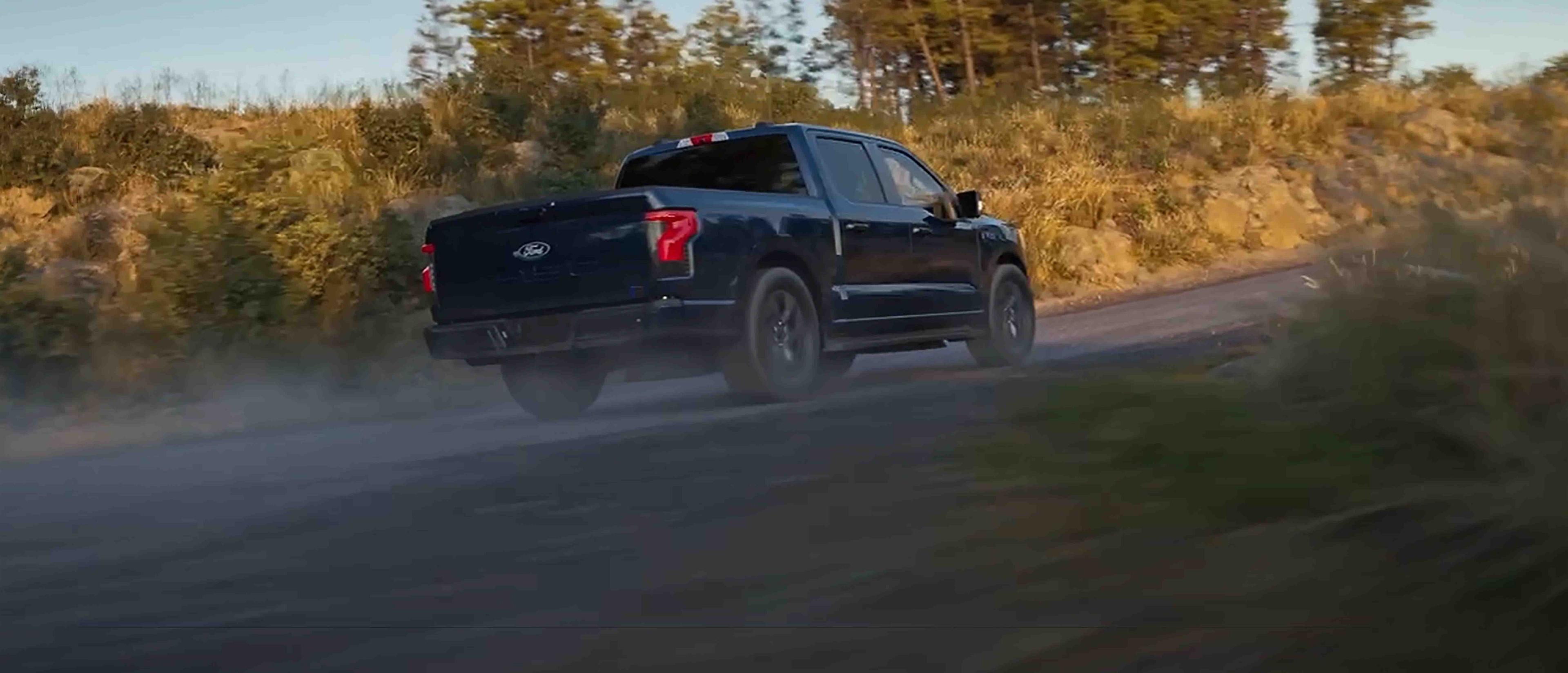 A black 2025 Ford F-150® Lightning® pickup driving on a gravel road, kicking up dust