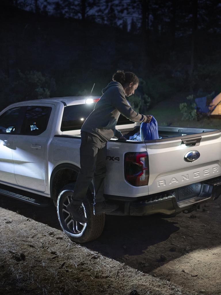 A person climbing into the bed of their 2026 Ford Ranger® truck to grab a backpack