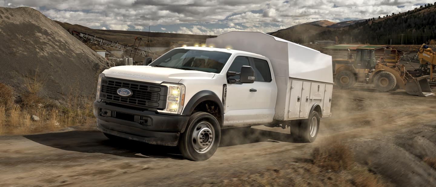 2025 Ford Super Duty® F-450® XL with a utility box driving up a dirt road jobsite
