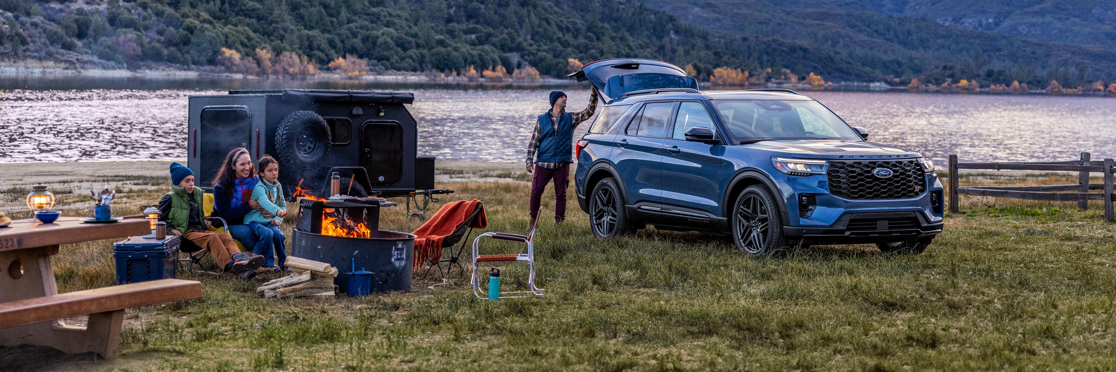 A 2025 Ford Explorer® ST SUV parked near the edge of a lake with a family at their camp site