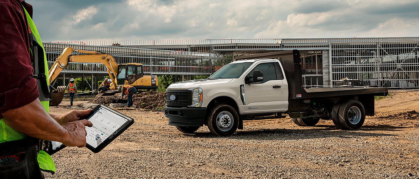 Worker using a tablet at construction site while a 2025 Ford Super Duty® Chassis Cab is parked in the background